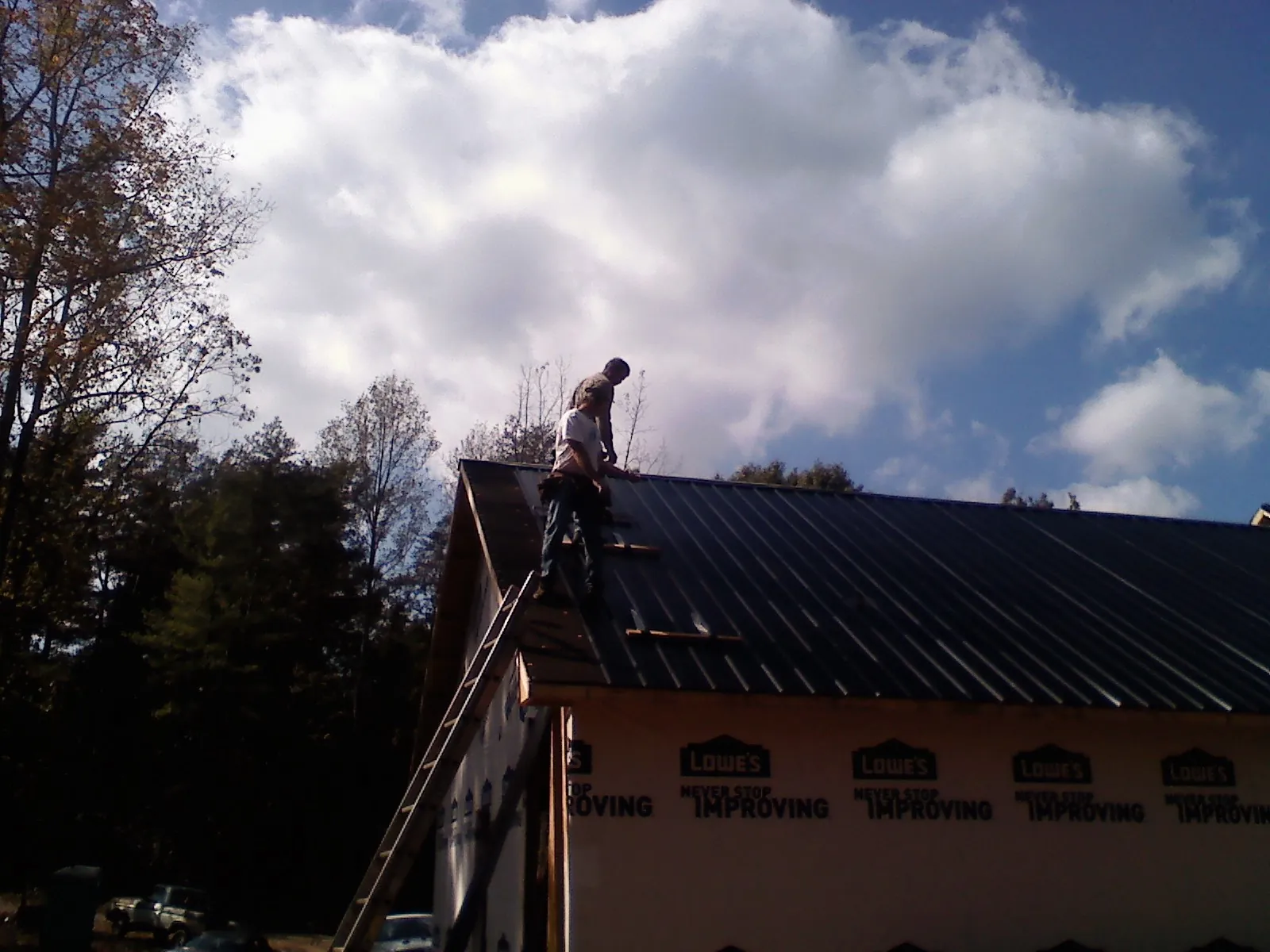 Roofer fastening dark metal panels high against a cloudy sky, from a Roof Inspection job in Everson